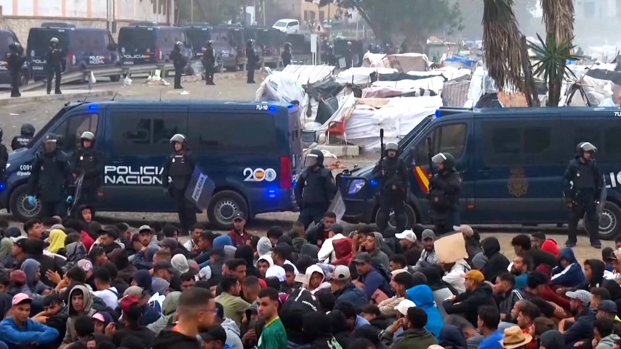 Migranten zitten op een kluitje op de grond tijdens ontruiming in Ceuta