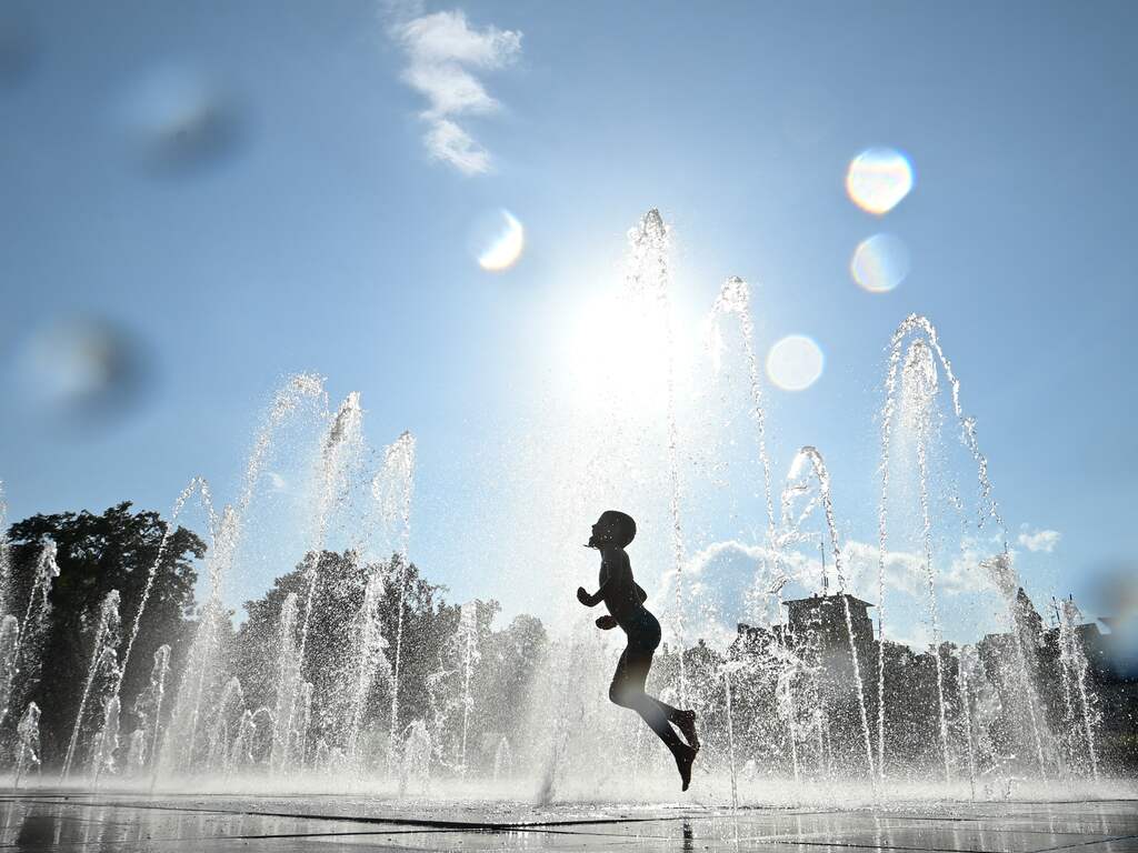Een jongetje zoekt verkoeling in een fontein tijdens een hete dag in Frankrijk.