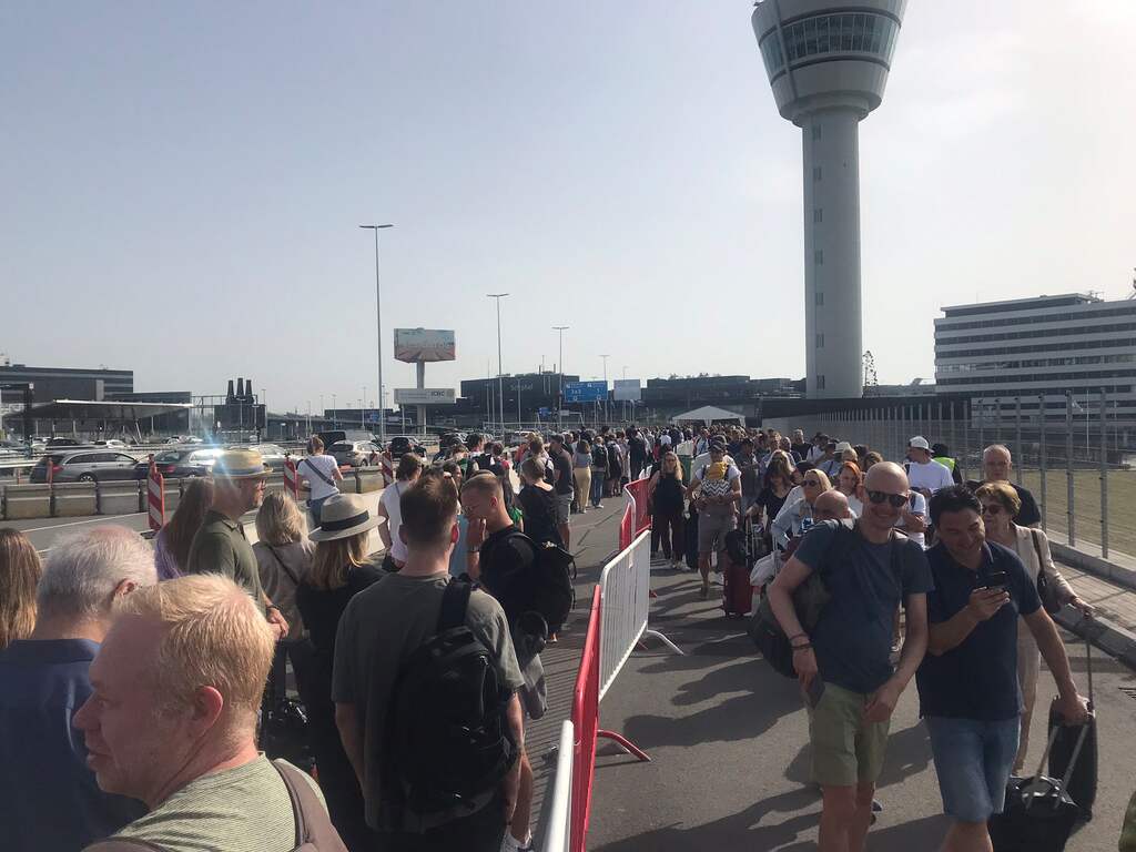 Reizigers wachten buiten in hitte voor Schiphol, medewerkers delen water uit