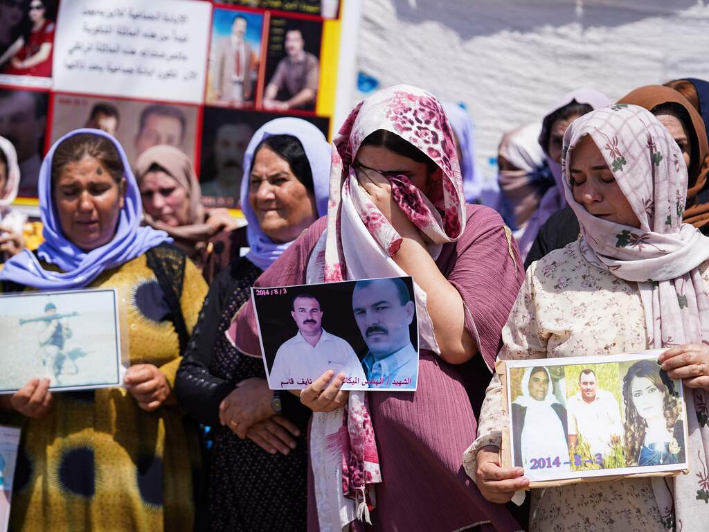 Iraqi Yazidi women cry as they hold pictures of their victims and missing relatives during a ceremony in Chamishko camp, in the Kurdistan Region of Iraq, marking the 10th anniversary of the Yazidi genocide.
